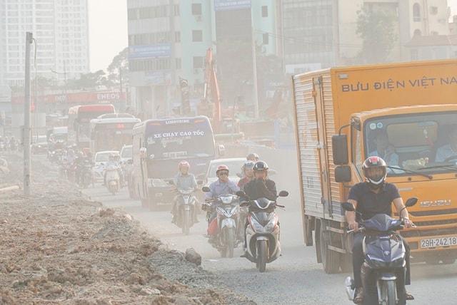 Người đi xe máy đeo khẩu trang di chuyển trên đường nhiều bụi gần công trình xây dựng tại Hà Nội.